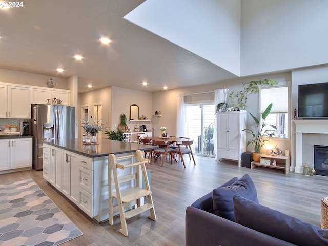 kitchen featuring white cabinetry, stainless steel fridge with ice dispenser, a tile fireplace, and light hardwood / wood-style flooring