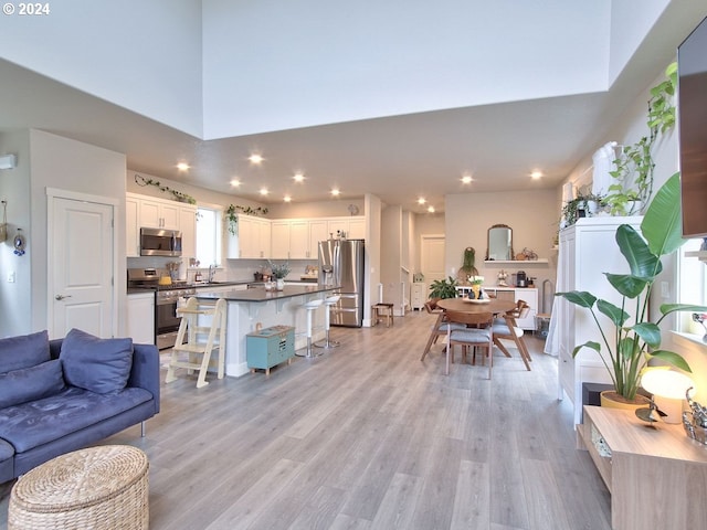 living room featuring plenty of natural light, sink, a high ceiling, and light hardwood / wood-style flooring