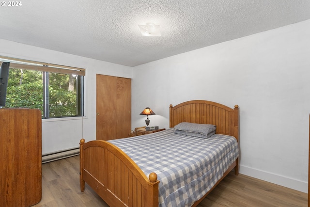 bedroom featuring a baseboard heating unit, light hardwood / wood-style floors, and a textured ceiling