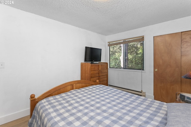 bedroom featuring a baseboard radiator, light wood-type flooring, a closet, and a textured ceiling