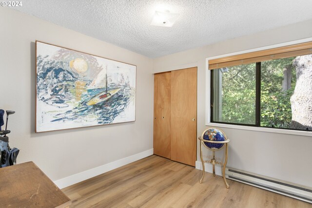 interior space with a baseboard heating unit, wood-type flooring, and a textured ceiling