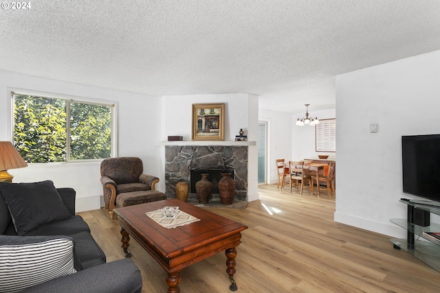 living room featuring a textured ceiling, a fireplace, light hardwood / wood-style flooring, and a notable chandelier