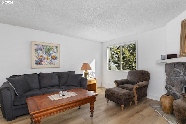 living room featuring a stone fireplace, a textured ceiling, and light hardwood / wood-style flooring