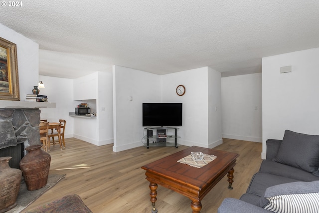 living room featuring light wood-type flooring, a textured ceiling, and a fireplace