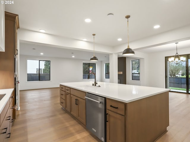 kitchen with a center island with sink, hanging light fixtures, sink, light wood-type flooring, and appliances with stainless steel finishes