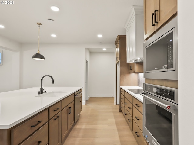 kitchen featuring sink, light wood-type flooring, hanging light fixtures, and appliances with stainless steel finishes