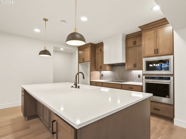 kitchen with a large island, sink, stainless steel appliances, pendant lighting, and light wood-type flooring