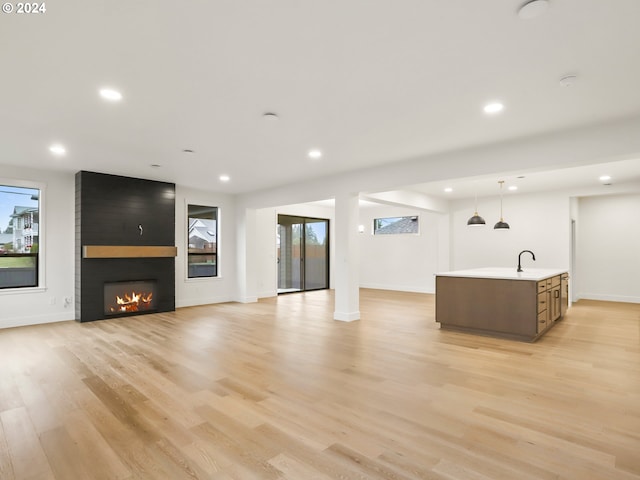 unfurnished living room featuring a large fireplace, sink, and light hardwood / wood-style flooring