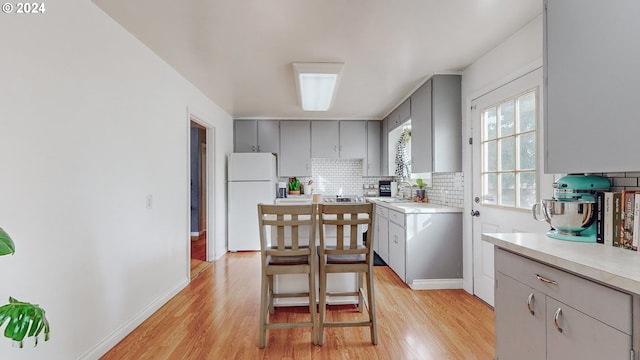 kitchen with white refrigerator, backsplash, light hardwood / wood-style floors, and gray cabinetry