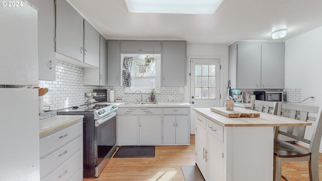 kitchen with white refrigerator, sink, stainless steel range with electric stovetop, a breakfast bar area, and light hardwood / wood-style floors