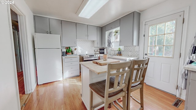 kitchen with tasteful backsplash, white fridge, electric stove, light hardwood / wood-style flooring, and gray cabinets