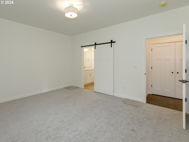 interior space with a barn door, light carpet, and ensuite bath