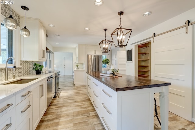 kitchen featuring a center island, a barn door, stainless steel appliances, white cabinetry, and wooden counters