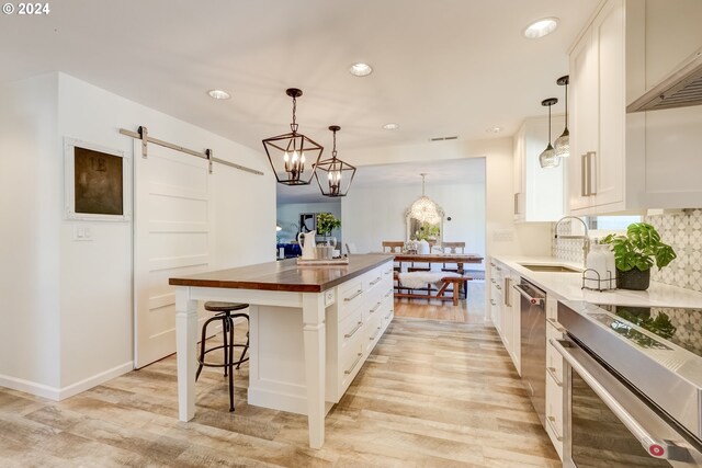 kitchen with a barn door, white cabinetry, an island with sink, wooden counters, and a kitchen breakfast bar