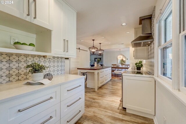 kitchen with decorative light fixtures, a wealth of natural light, decorative backsplash, and wall chimney exhaust hood