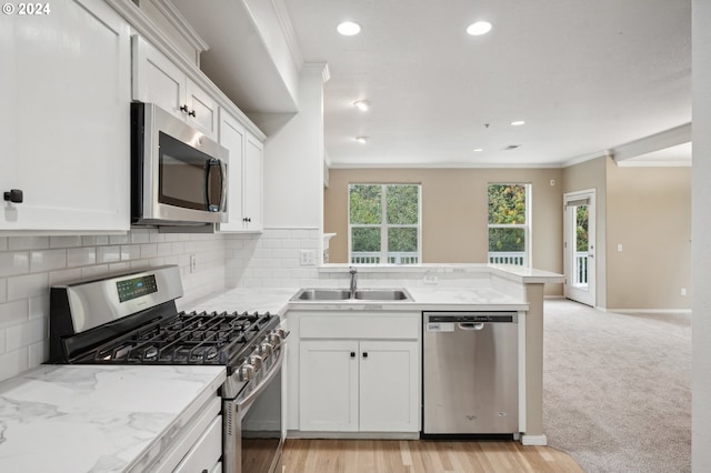 kitchen with light carpet, ornamental molding, stainless steel appliances, sink, and white cabinets