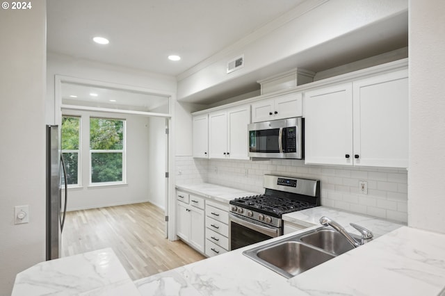 kitchen featuring light stone countertops, white cabinetry, sink, stainless steel appliances, and decorative backsplash