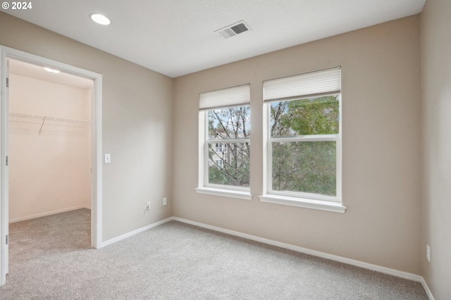 unfurnished bedroom with a walk in closet, light carpet, and a closet