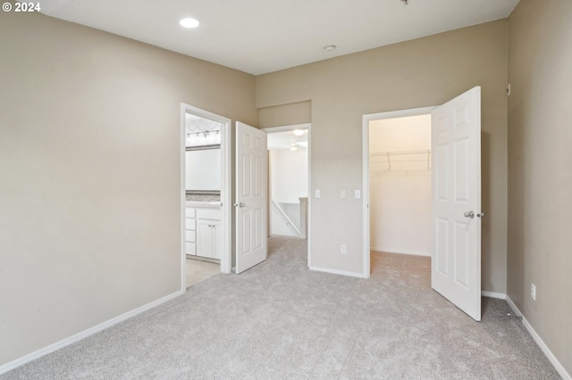 unfurnished bedroom with light colored carpet, a walk in closet, and a closet