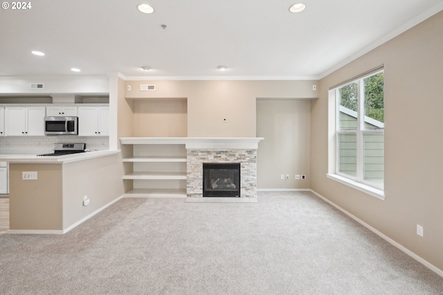 unfurnished living room with a stone fireplace, crown molding, and light carpet