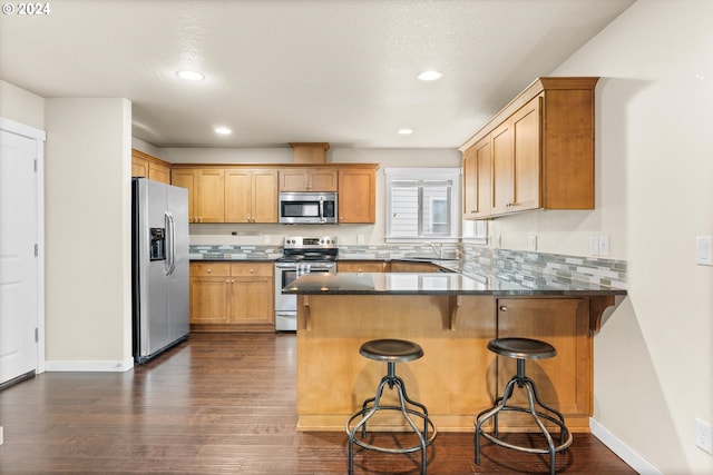 kitchen featuring kitchen peninsula, appliances with stainless steel finishes, dark hardwood / wood-style flooring, a breakfast bar, and dark stone countertops