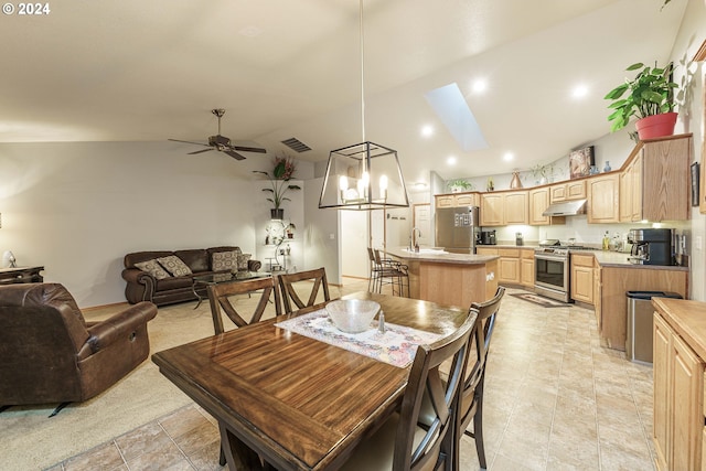 dining space featuring sink, ceiling fan with notable chandelier, and vaulted ceiling with skylight