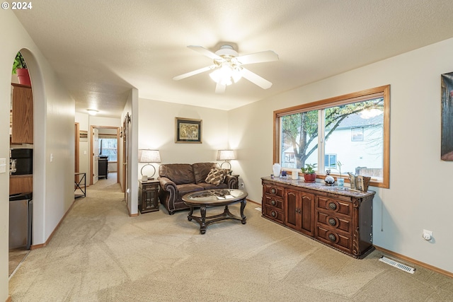 living area featuring ceiling fan, light colored carpet, and a textured ceiling