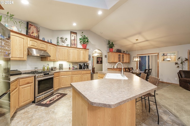 kitchen with gas stove, sink, hanging light fixtures, vaulted ceiling, and a center island with sink