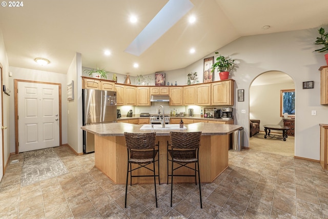 kitchen with a kitchen bar, stainless steel fridge, lofted ceiling with skylight, a kitchen island with sink, and sink