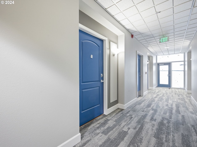 hall with dark colored carpet and a drop ceiling