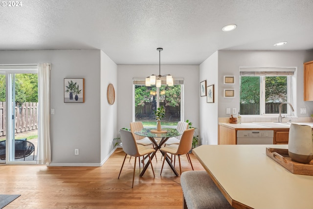 dining space featuring a textured ceiling, light wood-type flooring, sink, and an inviting chandelier