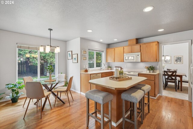 kitchen with white appliances, a textured ceiling, pendant lighting, light hardwood / wood-style floors, and a kitchen island