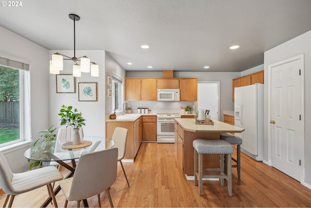 kitchen with pendant lighting, white appliances, light hardwood / wood-style flooring, and plenty of natural light