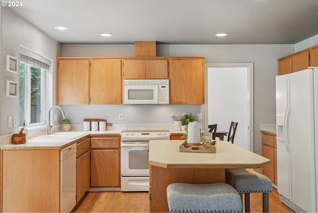 kitchen with a breakfast bar, sink, light hardwood / wood-style flooring, and white appliances