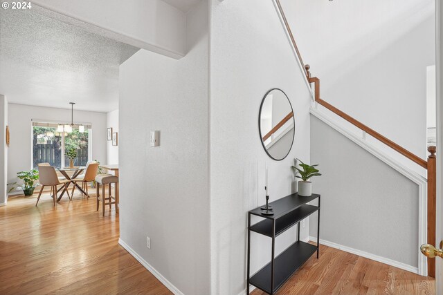 hall with light wood-type flooring, a chandelier, and a textured ceiling