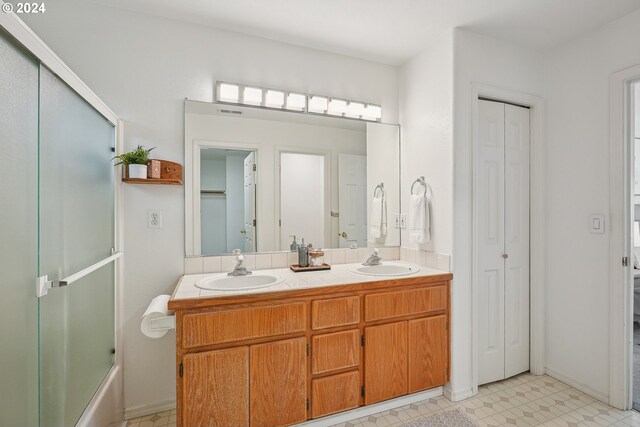 bathroom with combined bath / shower with glass door, tile patterned floors, and double sink vanity