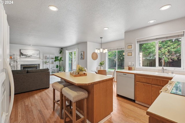 kitchen with hanging light fixtures, white dishwasher, sink, white cabinetry, and light hardwood / wood-style flooring