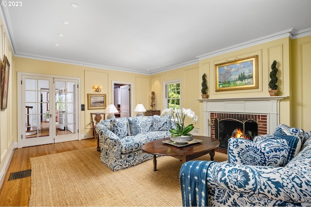 living room with french doors, ornamental molding, a brick fireplace, and light wood-type flooring