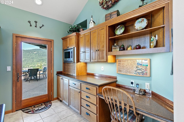 kitchen featuring stainless steel microwave, light tile patterned floors, and vaulted ceiling