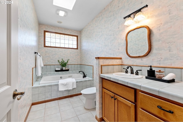 bathroom featuring a skylight, vanity, a relaxing tiled tub, tile patterned flooring, and toilet