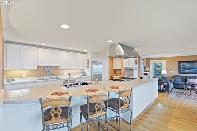 kitchen with white cabinets, sink, light hardwood / wood-style floors, island range hood, and stainless steel appliances