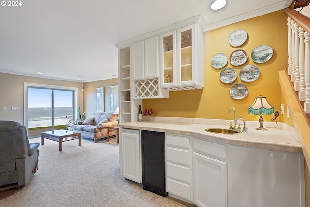 kitchen with tile counters, a water view, white cabinetry, and sink