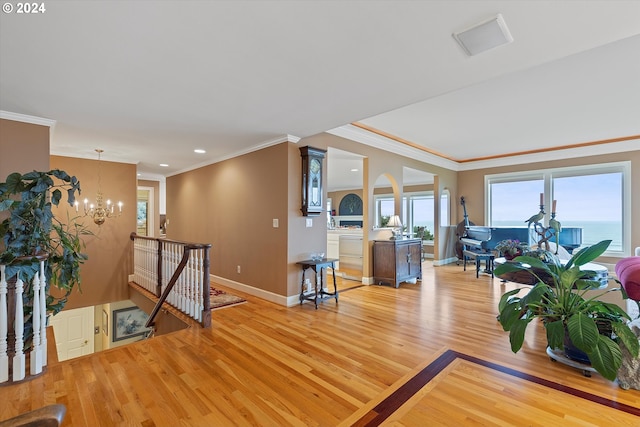 living room featuring a notable chandelier, a water view, light wood-type flooring, and crown molding