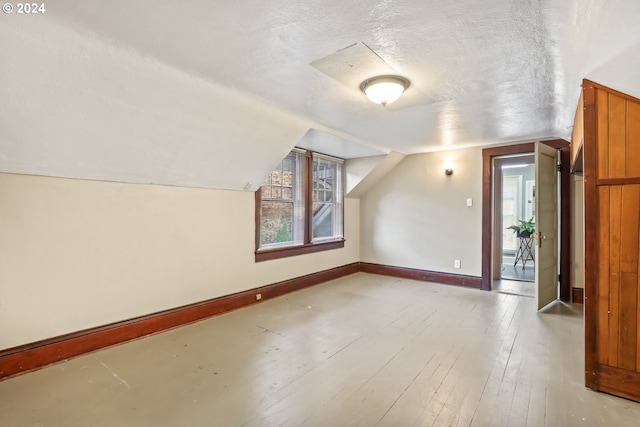 additional living space featuring a textured ceiling, light hardwood / wood-style floors, and lofted ceiling