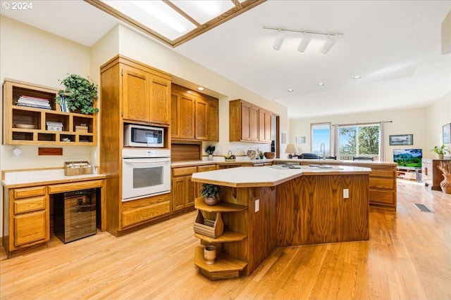 kitchen featuring beverage cooler, rail lighting, light hardwood / wood-style flooring, a center island, and white appliances