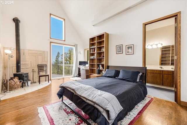 bedroom featuring light hardwood / wood-style flooring, a wood stove, high vaulted ceiling, and access to outside