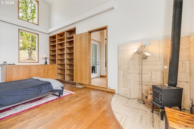 bedroom with a towering ceiling, hardwood / wood-style flooring, and a wood stove