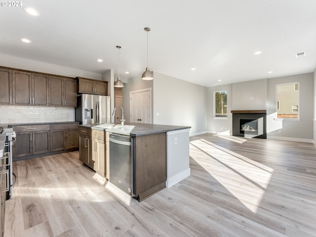 kitchen with sink, light wood-type flooring, stainless steel appliances, and a kitchen island with sink