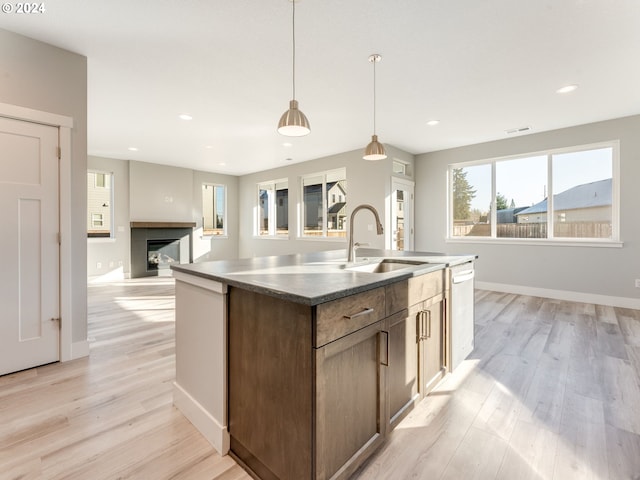 kitchen featuring a center island with sink, sink, hanging light fixtures, stainless steel dishwasher, and light hardwood / wood-style floors