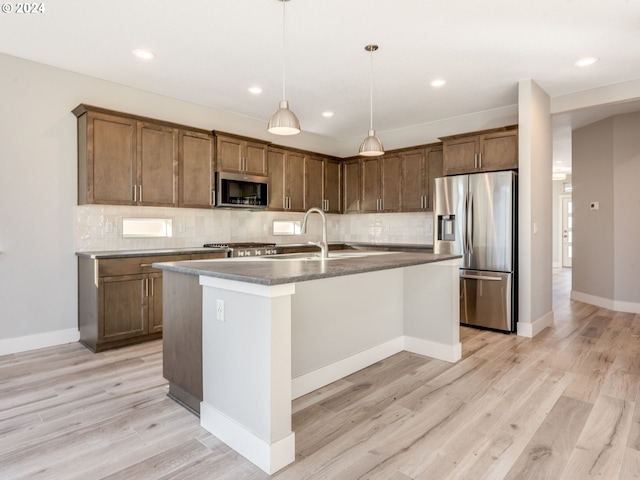 kitchen with sink, stainless steel appliances, pendant lighting, a center island with sink, and light wood-type flooring